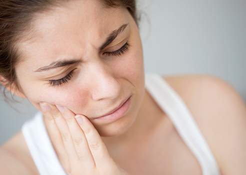 Woman holding her hand to her painful jaw before receiving botox for tmj at  Placentia Oral Surgery in Placentia, CA