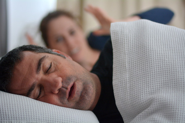 Male patient from Placentia Oral Surgery snoring in bed while woman covers her ears in Placentia, CA